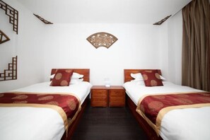 Hotellihuone, jossa on kaksi sänkyä, niiden välissä puinen yöpöytä ja sänkyjen yläpuolella koristeellinen seinätaulu.