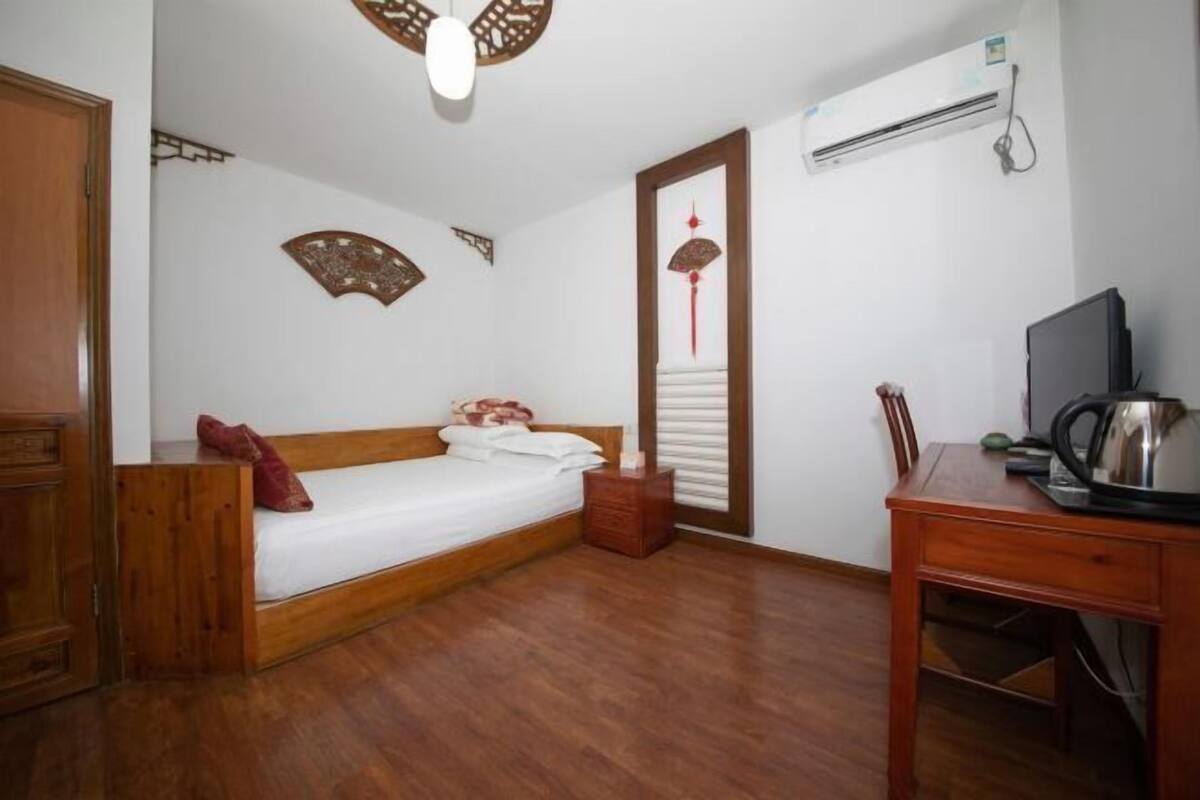 Ein Schlafzimmer mit einem hölzernen Bett, einem Schreibtisch, einem Sessel, einer Klimaanlage und Wanddekoration.