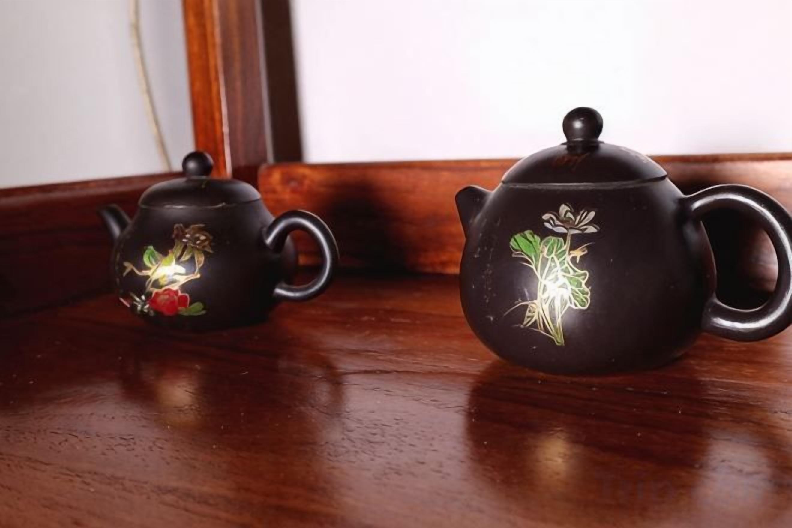 Zwei schwarze Keramiktöpfe mit floralen Mustern auf einer Holztischplatte.