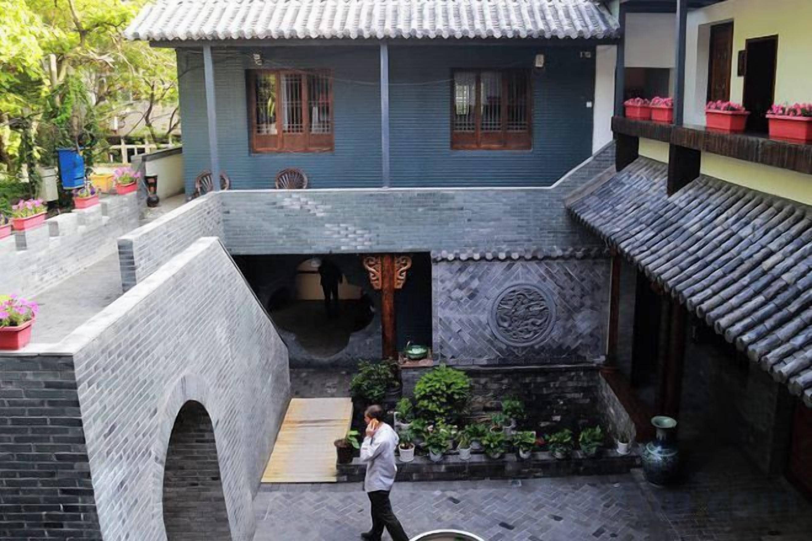A courtyard with a traditional building, a brick wall, and potted plants.