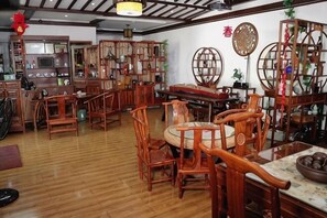 A traditional wooden interior with multiple dining tables and chairs, a piano, and decorative wall pieces.