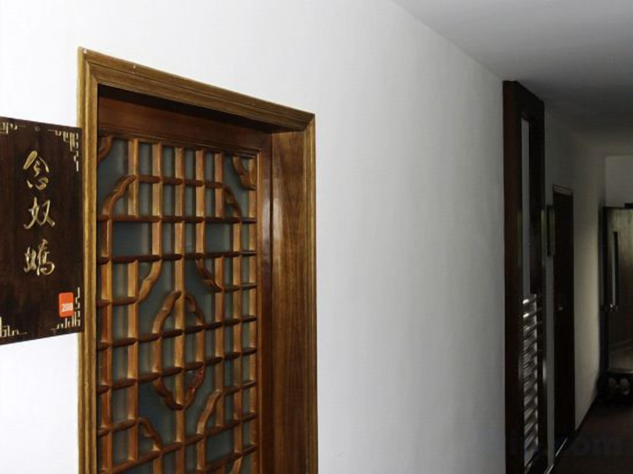Une porte en bois ornée d’un motif de treillis complexe, un couloir au plancher sombre et une enseigne fixée au mur avec du texte.