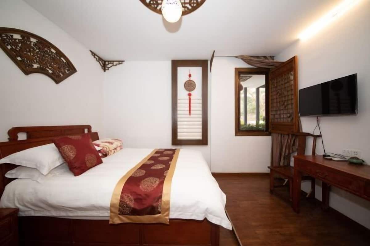 Ein Schlafzimmer mit einem hölzernen Bett, weißer Bettwäsche, einem roten Zierkissen, einem an der Wand montierten Fernseher und einem Holzschreibtisch.