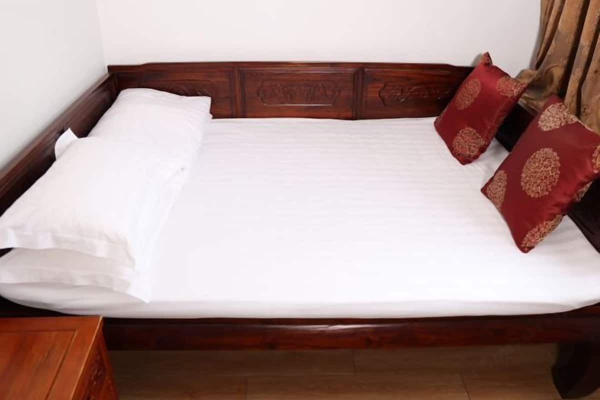 Ein ordentlich bezogenes Bett mit weißen Laken und zwei roten Kissen mit Goldmustern, in einem hölzernen Bettrahmen.