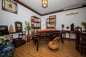 A traditional room with a wooden floor, a sofa, a bookshelf, a piano, and a decorative lamp.