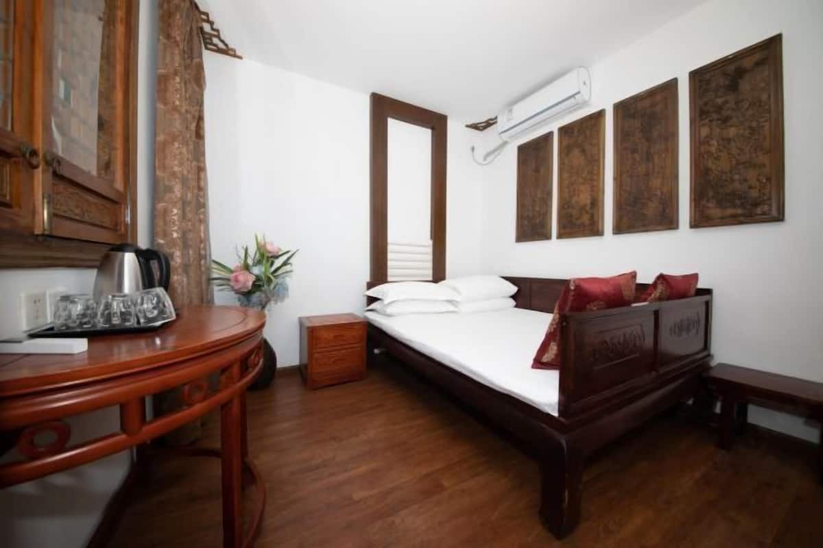 Ein Schlafzimmer mit einem hölzernen Bett, einem Nachttisch mit Wasserkocher und einem kleinen Holzbeistelltisch.