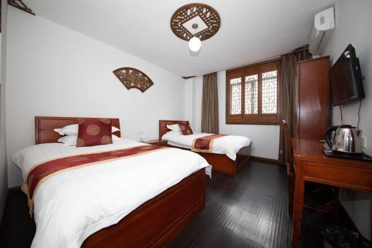 Ein Hotelzimmer mit zwei hölzernen Betten, einem Holztisch, einem Fernseher und einem Fenster mit Vorhängen.