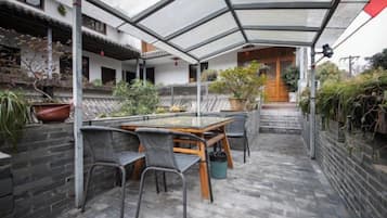 A covered patio area with a table and chairs, surrounded by plants and a brick wall.