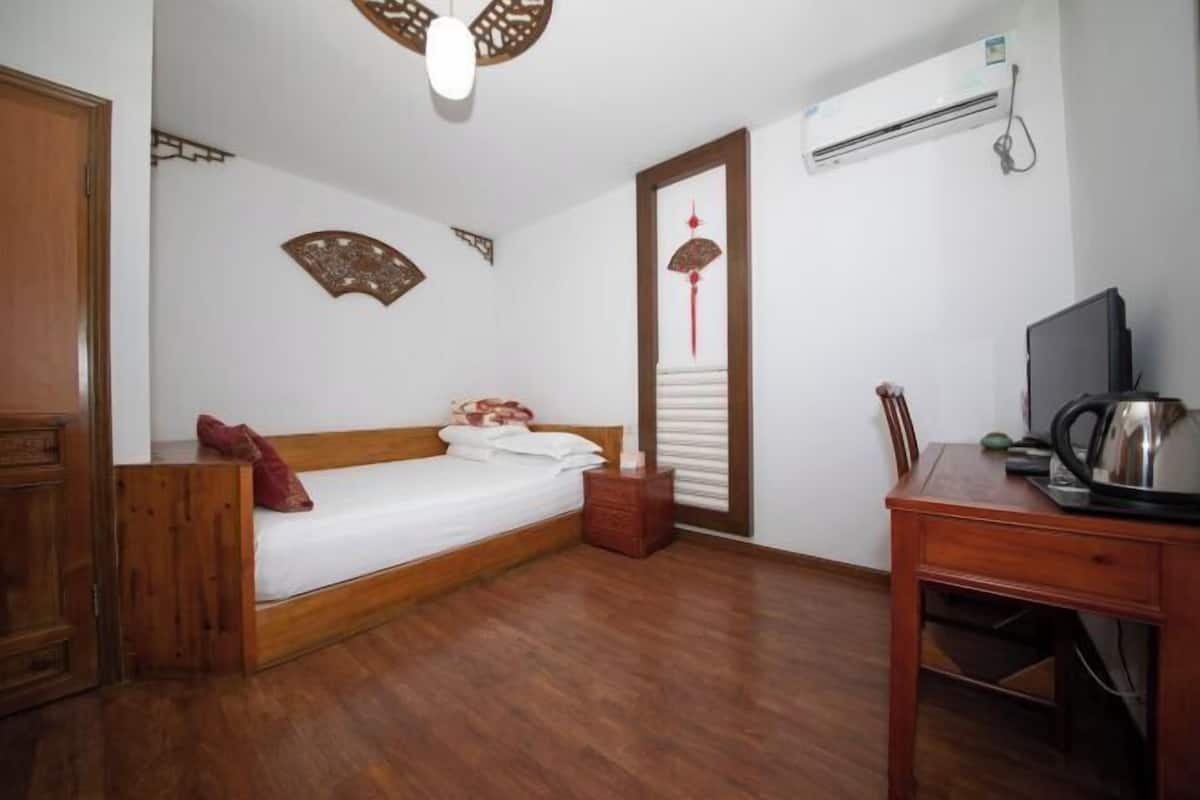 Ein Schlafzimmer mit einem hölzernen Bett, einem Schreibtisch, einer Klimaanlage und dekorativen Wandbildern.