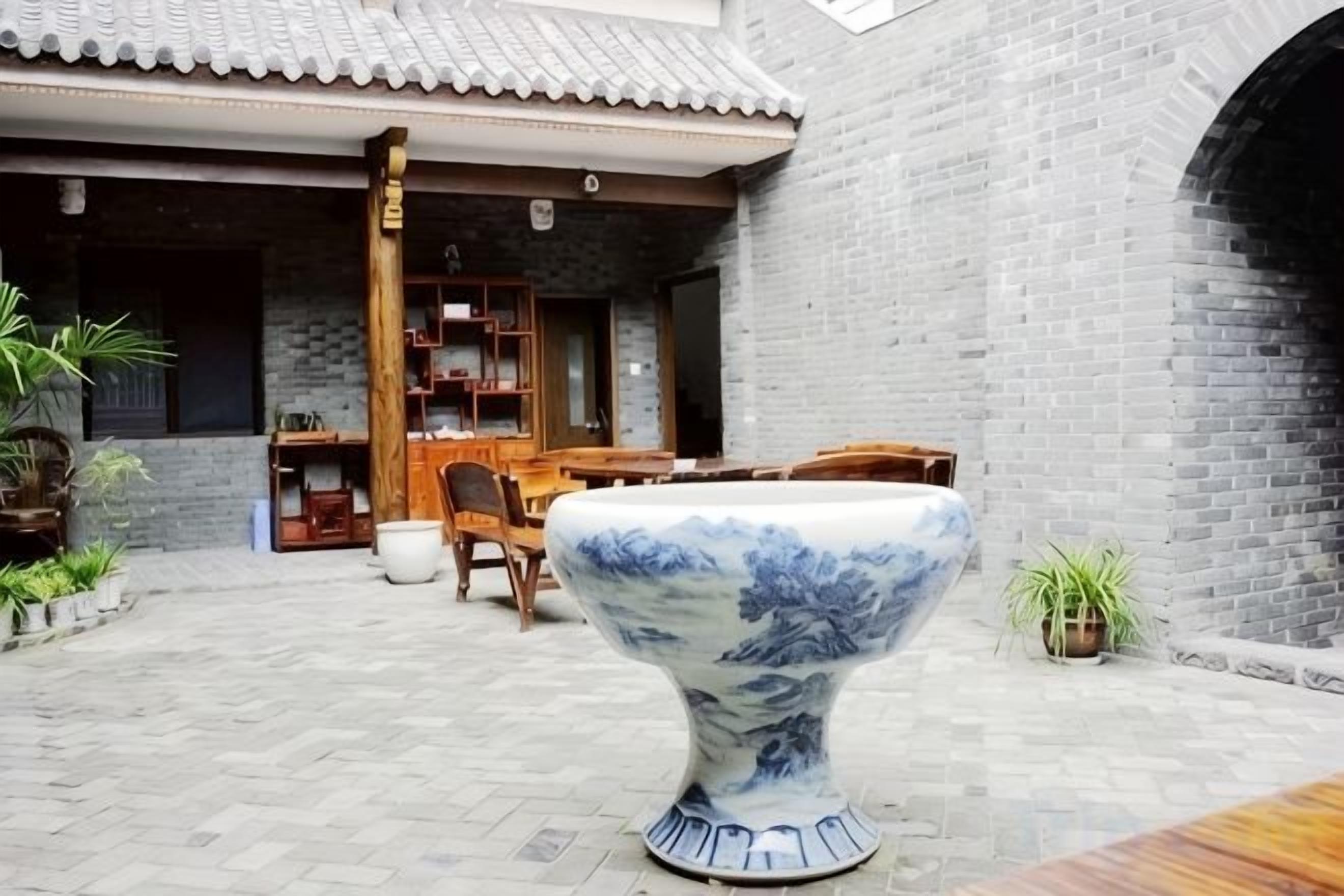 A courtyard with a tiled floor, a wooden table, chairs, and a large decorative bowl.