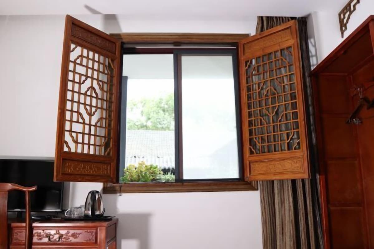 A room with a traditional wooden door, a window with a view of greenery, and a desk with a kettle.
