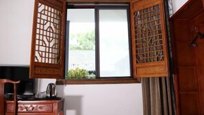 A room with a traditional wooden door, a window with a view of greenery, and a desk with a kettle. - Shaoxing Dayue Xiaoyuan Culture Theme Hotel (Lu Xun's hometown Shenyuan Branch) (Shaoxing)