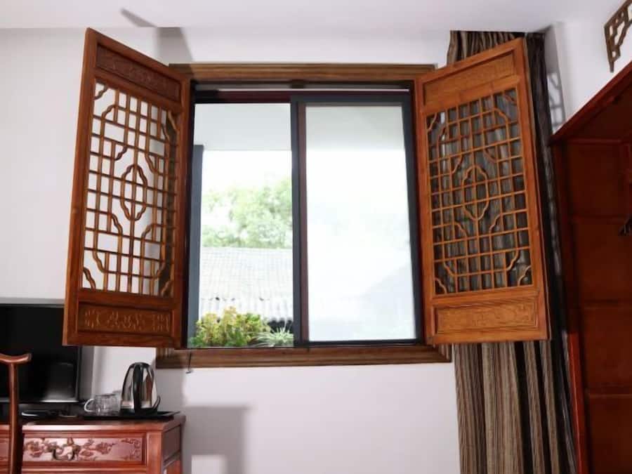 Quarto com porta de madeira tradicional, janela com vista para vegetação e escrivaninha com chaleira.