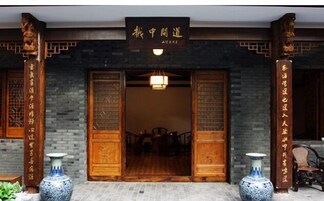 Entrada de un edificio tradicional chino, con puertas de madera, un letrero y dos jarrones.