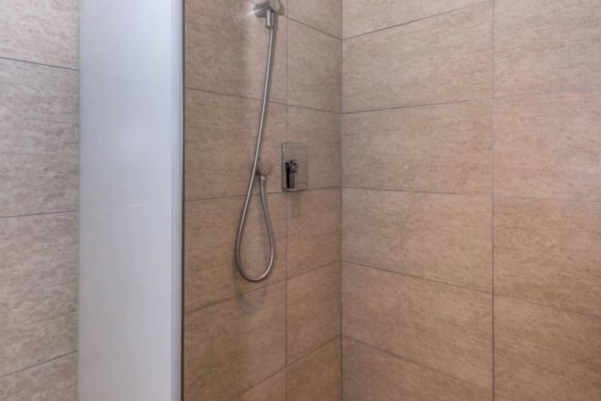 A shower area with a handheld showerhead and a wall-mounted control panel.