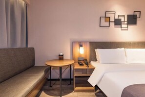 A hotel room with a bed, a sofa, a small round table with a lamp, a nightstand with a phone, and a wall-mounted light fixture. - Homeinn Plus Hotel (Beijing Jianguomen Capital Pediatric Institute) (Beijing)
