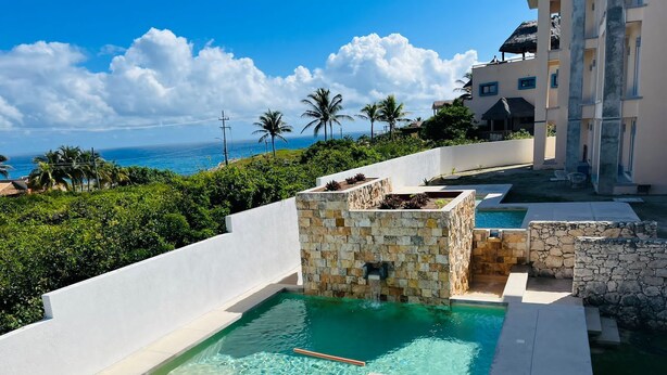 A pool area with a stone structure, clear water, and a view of the ocean. - La Diosa Condos holiday apartment (Isla Mujeres)