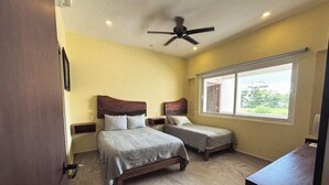 A bedroom with two beds, a ceiling fan, and a window with a view of greenery. - La Diosa Condos holiday apartment (Isla Mujeres)