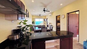 A kitchen with a central island, a ceiling fan, and a view of the ocean through large windows. - La Diosa Condos holiday apartment (Isla Mujeres)