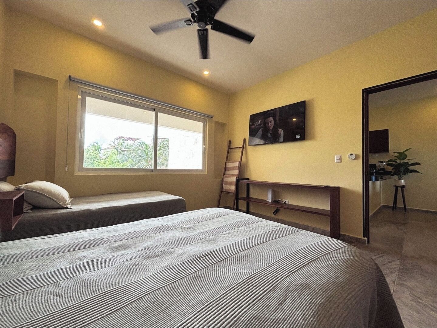 A bedroom with a bed, a desk, a TV, and a window.