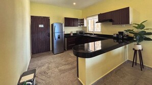 A kitchen with a central island, dark wooden cabinets, a stainless steel refrigerator, and a window providing natural light. - La Diosa Condos holiday apartment (Isla Mujeres)