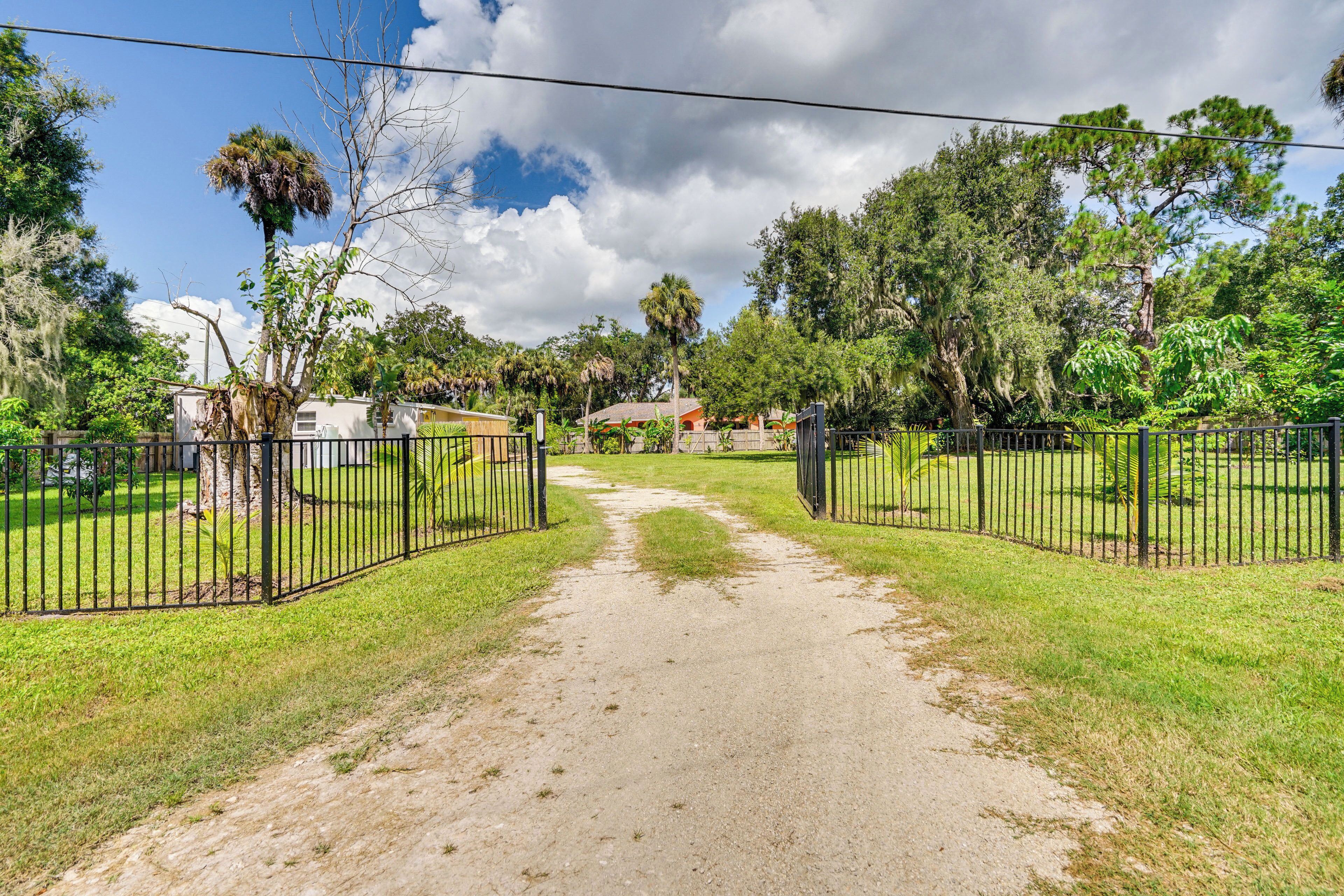 A paved pathway leading to a gated area with lush greenery and trees.
