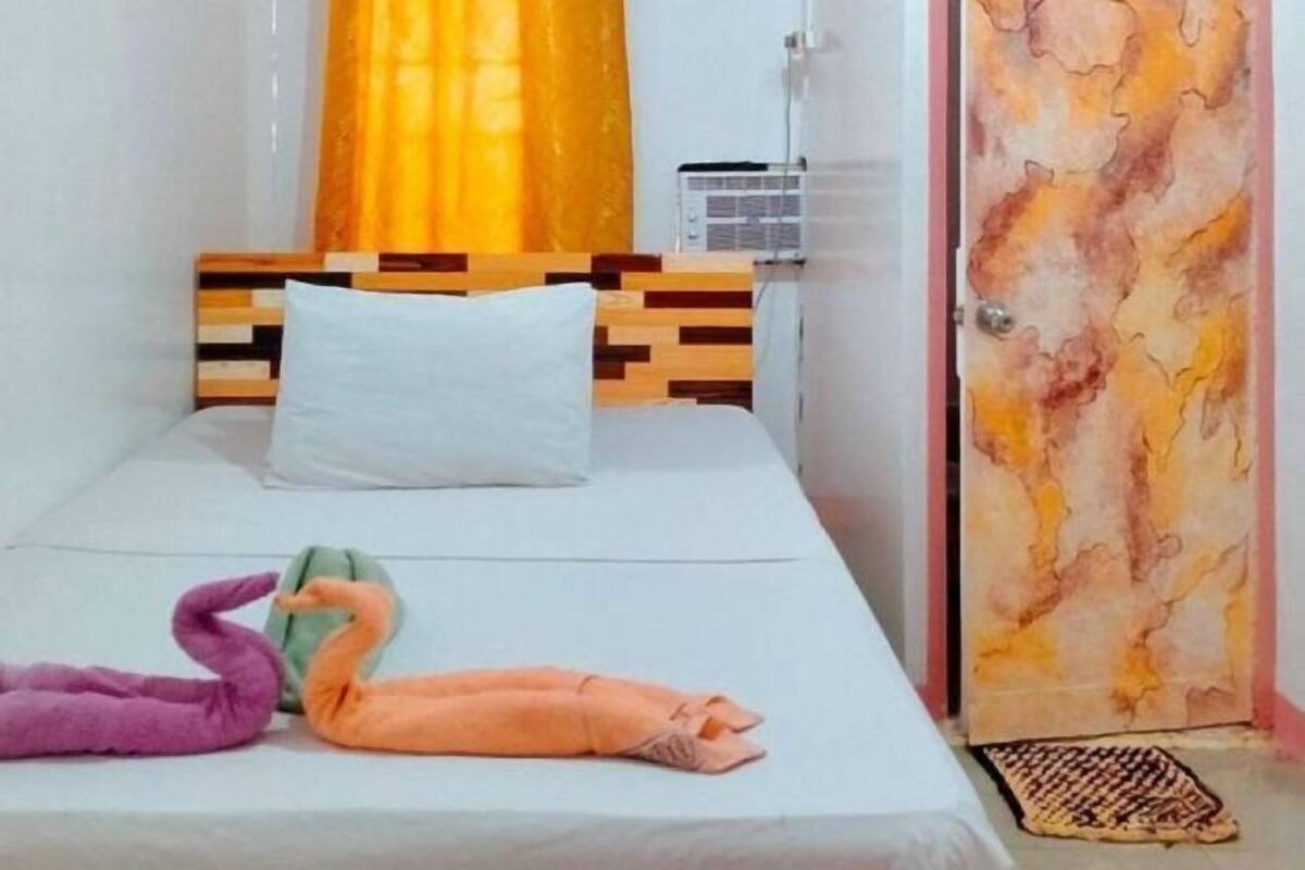 A single bed with a wooden headboard, a white pillow, and two swan-shaped pillows.