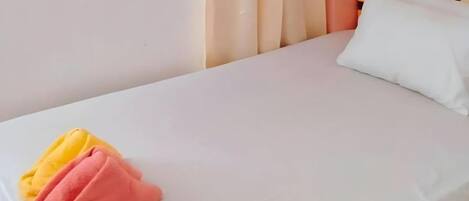 A bed with a white sheet, a pillow, and two folded towels.