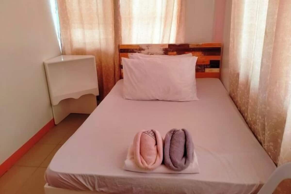 A single bed with a wooden headboard, a white pillow, and two rolled towels on the bed.