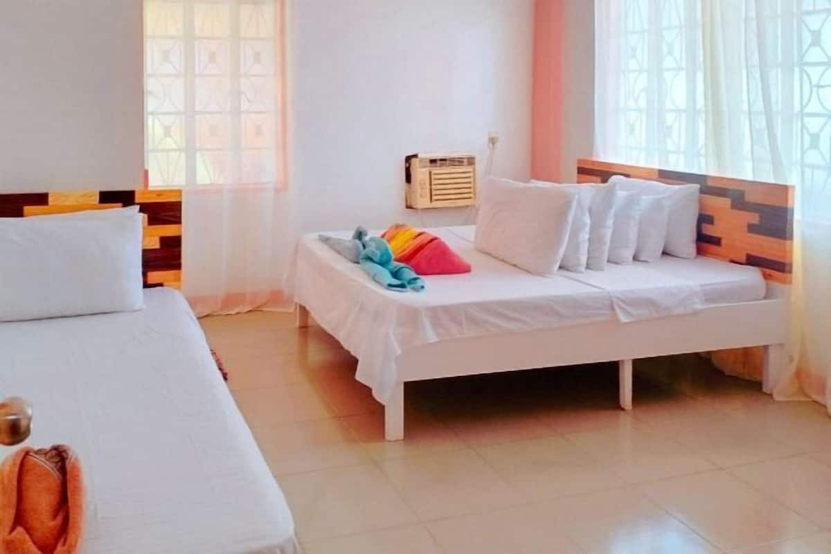 A hotel room with a bed, a bedside table, a window with curtains, and a wall-mounted heater.