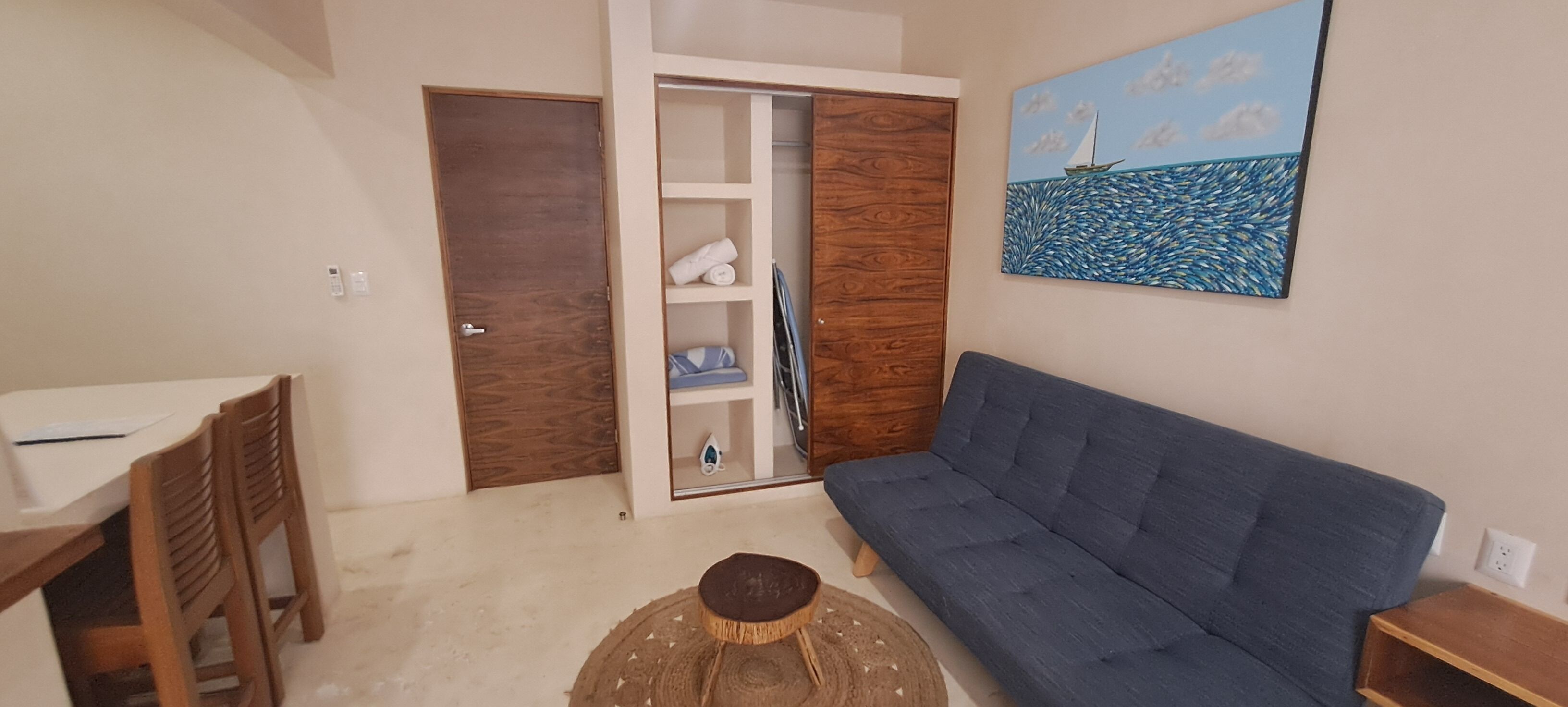 Un salón con un sofá azul, muebles de madera, un armario blanco y un cuadro de un velero.