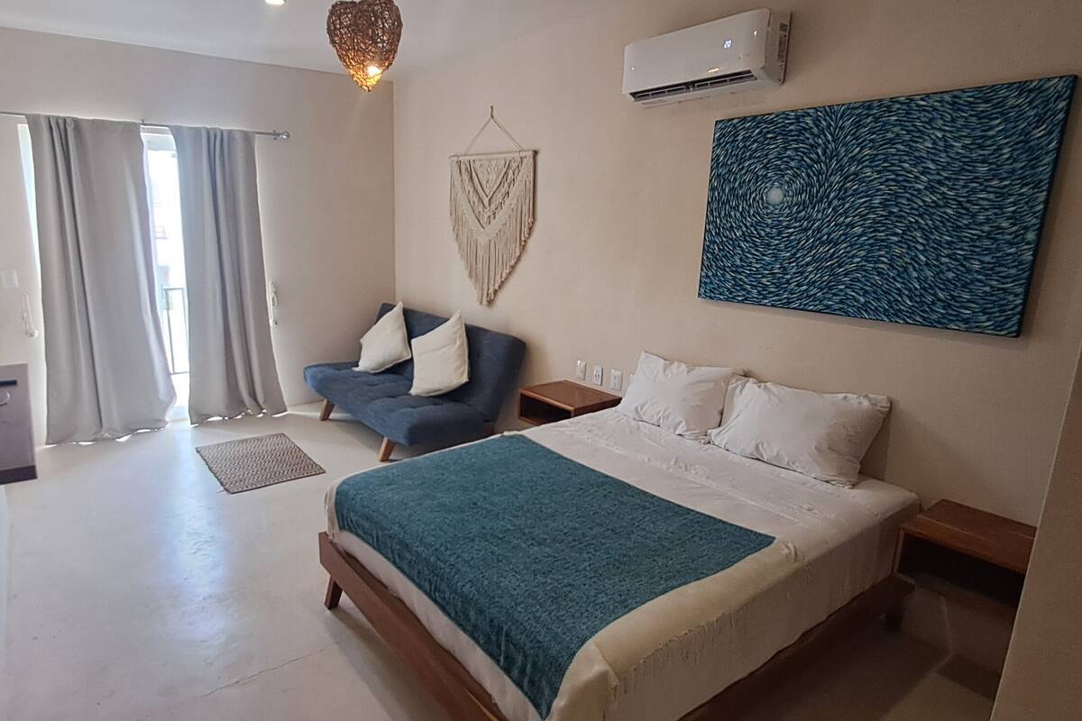 Une chambre à coucher comprenant un lit, une chaise, un climatiseur fixé au mur et une grande fenêtre avec des rideaux.