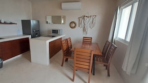 Eine kompakte Küche mit Kühlschrank, Mikrowelle und Spüle, ein Essbereich mit Holzsesseln und ein Fenster mit Vorhängen.