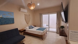 Ein Schlafzimmer mit einem Bett, einem blauen Sofa, einem Bild eines Segelboots, einem Wandbehang aus Makramee und einem an der Wand befestigten Fernseher.