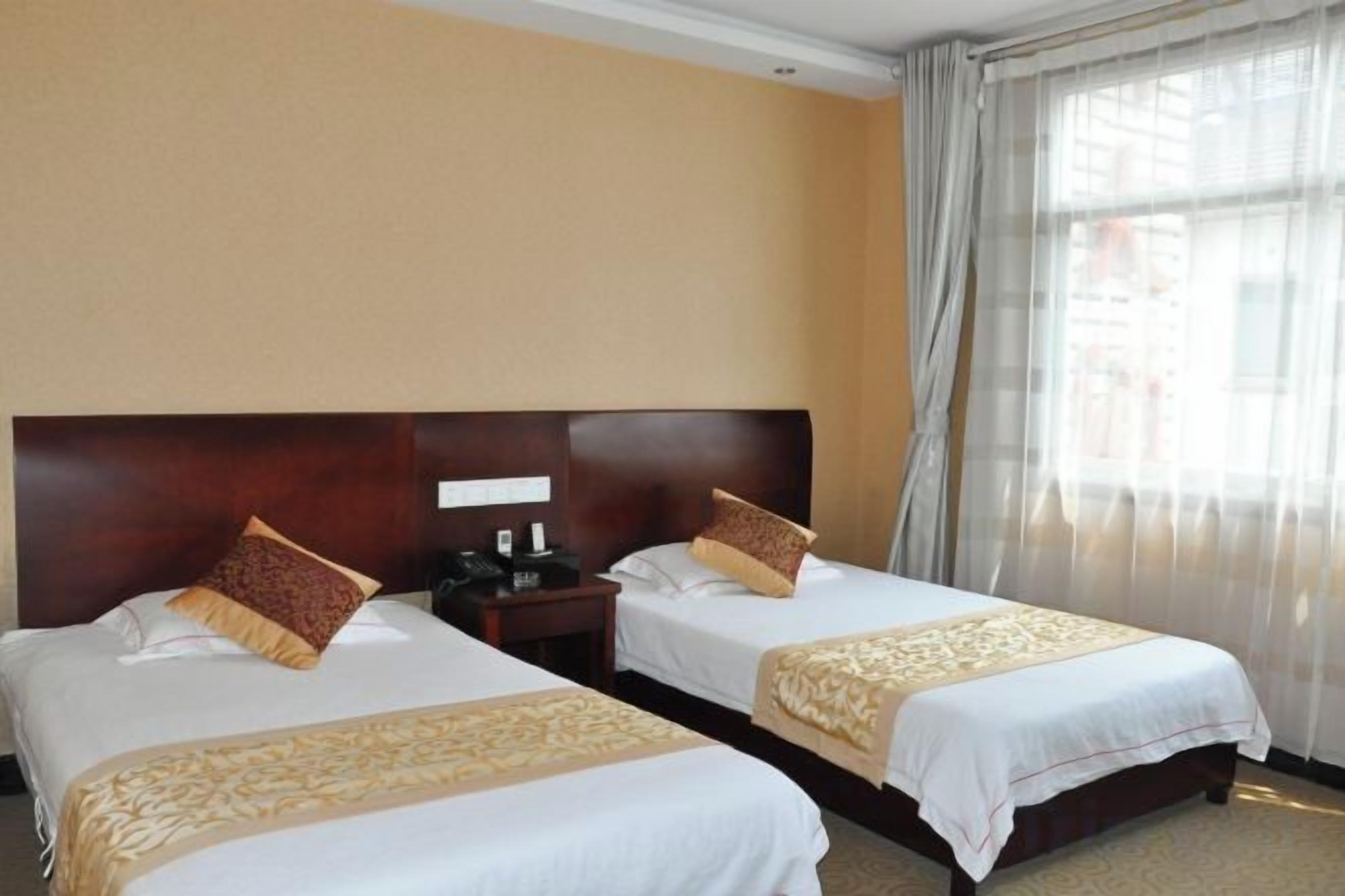 A hotel room with two beds, each with a wooden headboard, a nightstand, and a telephone.