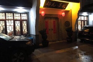 Entrada de un edificio tradicional chino con un portón de tejas, un farol rojo y un coche negro estacionado al frente.