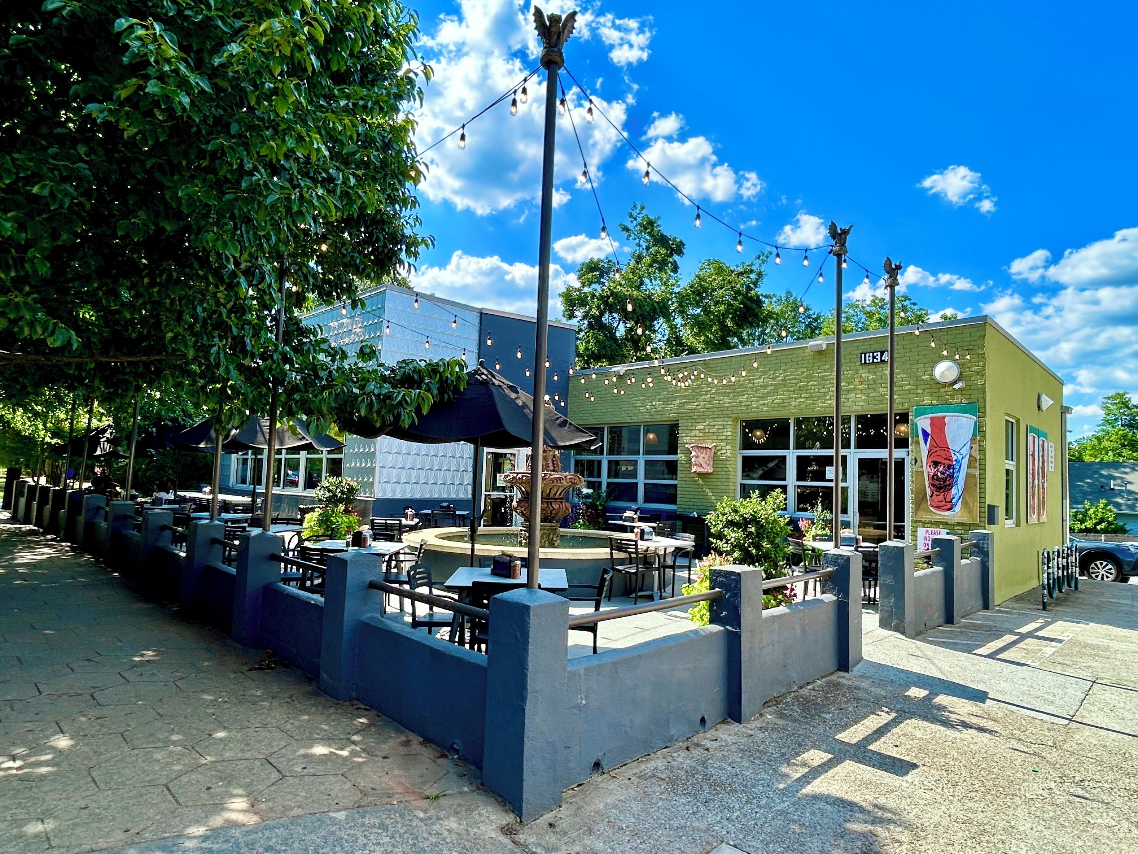 An outdoor seating area with tables and chairs, a fountain, and a building with a mural.
