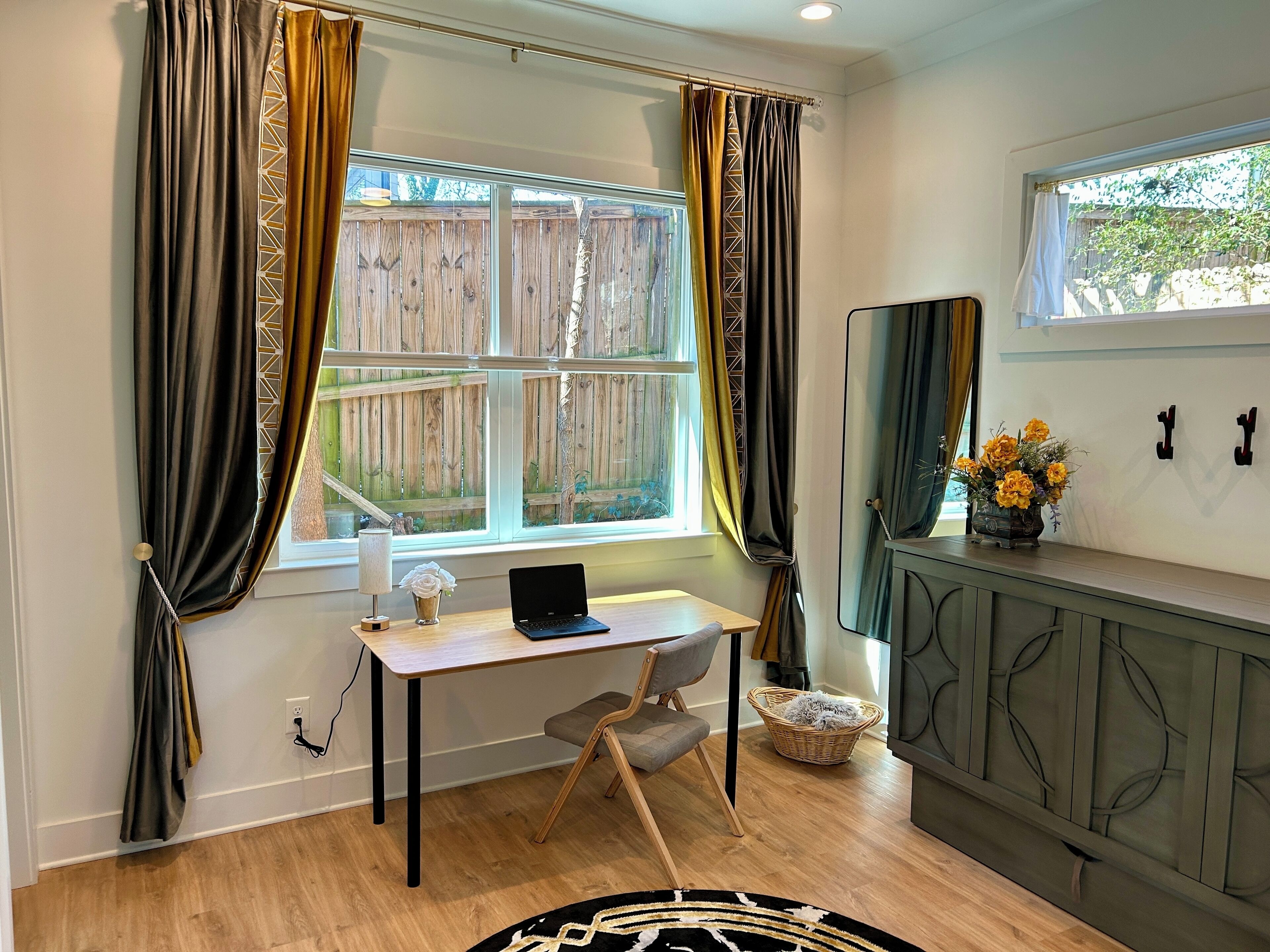 Ein Zimmer mit Schreibtisch, Laptop und einem fensterbündigen Vorhang.