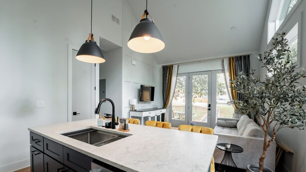 A modern kitchen with a central island, black cabinets, and a large window with curtains. - Inner City Hideout: Serenity with Big Nature Views (Atlanta)