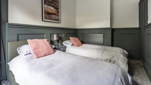 Quarto de hotel com duas camas, uma mesinha de cabeceira, abajur e uma grande pintura abstrata na parede.