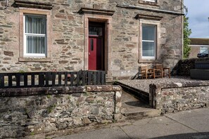 Un bâtiment en pierre avec une porte rouge, deux fenêtres et une clôture en bois.