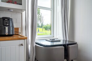 Eine kleine Küche mit Kaffeemaschine, einem Tisch mit Notizbuch und Blick auf eine grüne Landschaft durch ein Fenster.