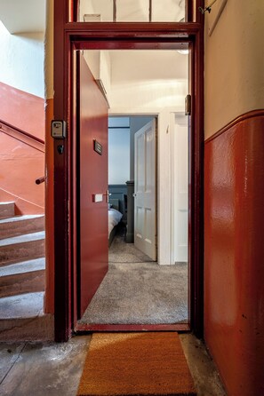 L’entrée d’un hôtel, avec une porte rouge, un paillasson et un escalier menant à une chambre équipée d ’un lit et d’un bureau.
