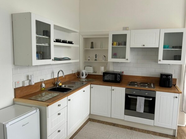 A modern kitchen with white cabinetry, a built-in microwave, a coffee maker, and a stove.