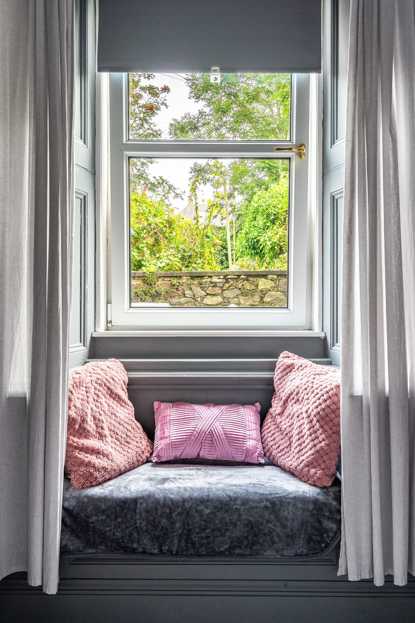 A window seat with a stone wall view, curtains, and pillows.