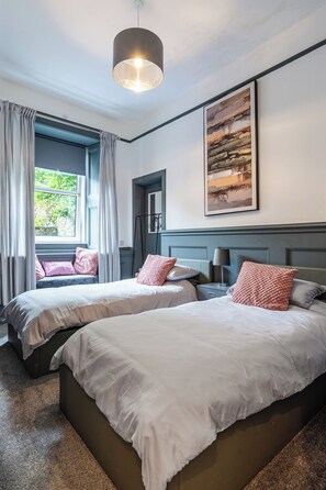 Ein Hotelzimmer mit zwei Betten, einem großen Fenster mit Vorhängen, einem Gemälde an der Wand und einer Pendelleuchte.