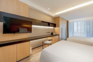 A modern hotel room with a large bed, a flat-screen TV mounted on the wall, a small seating area, and a large window with curtains.