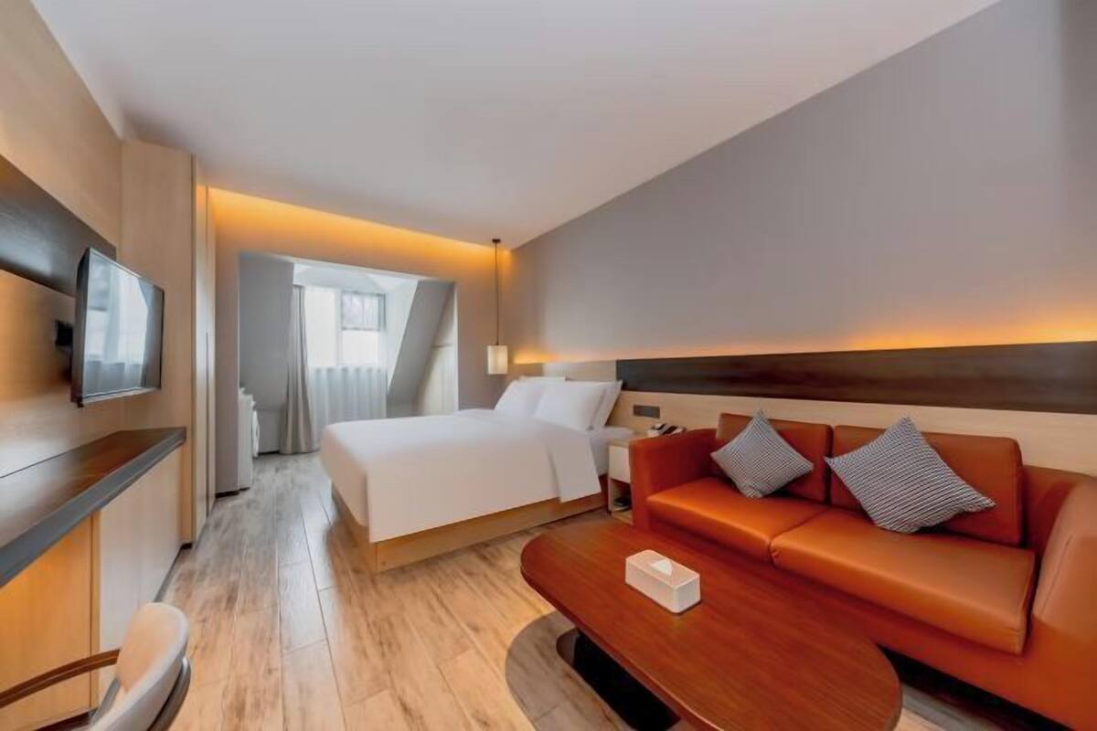 A hotel room with a bed, a sofa, a TV, and a desk.