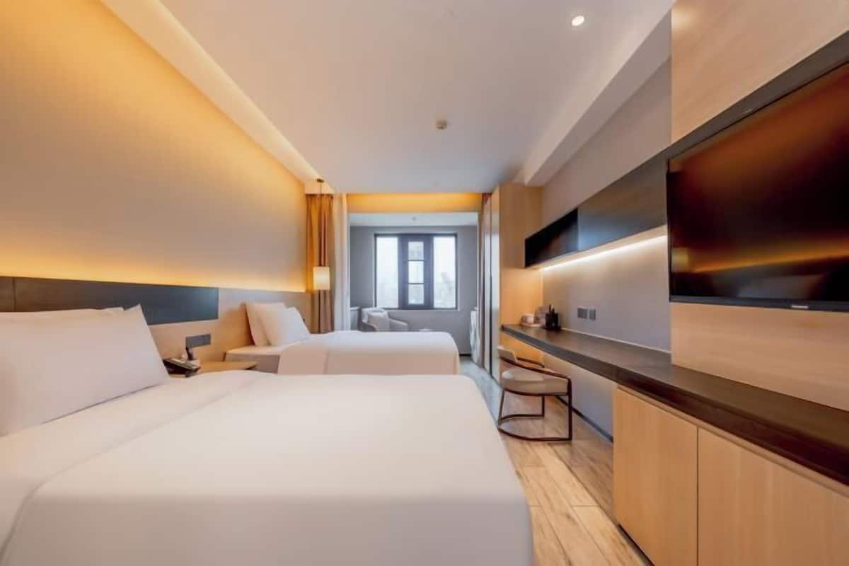 A hotel room with two beds, a TV, a desk, and a view of the hallway.