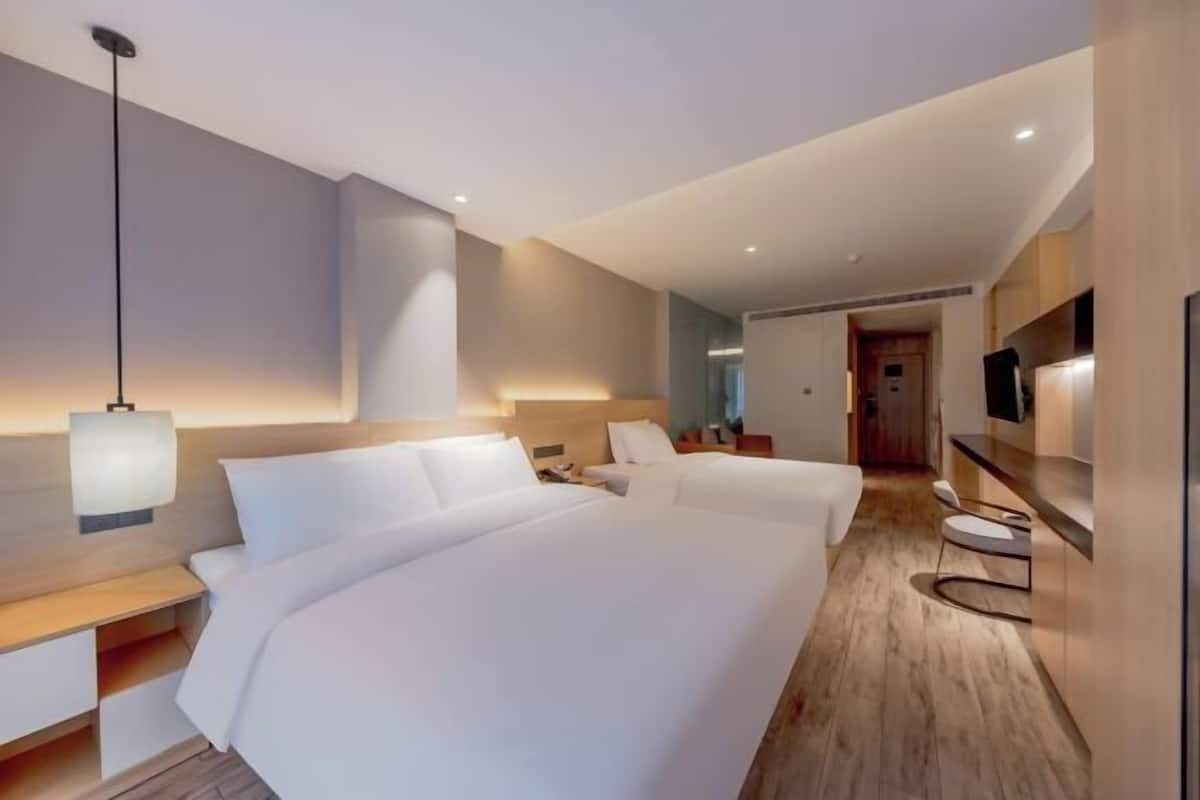 A modern hotel room with a large bed, bedside tables, a TV, and a desk.